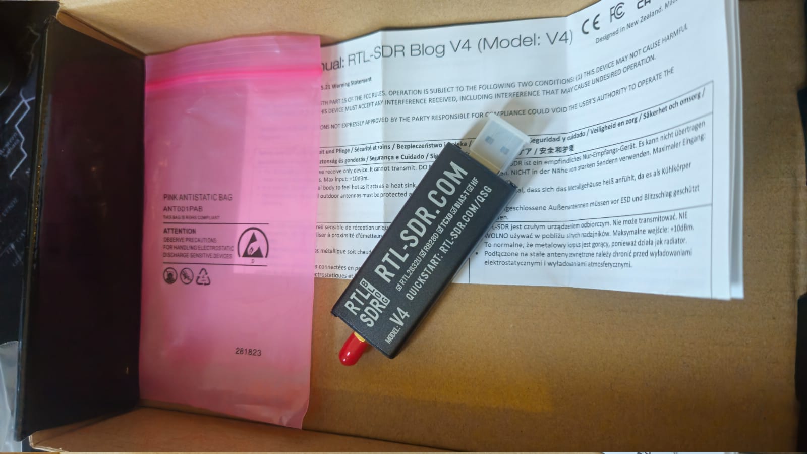 Dongle RTL-SDR Blog V4 sobre o manual impresso, com R828D, TCXO, bias tee e HF serigrafados na caixa de alumínio